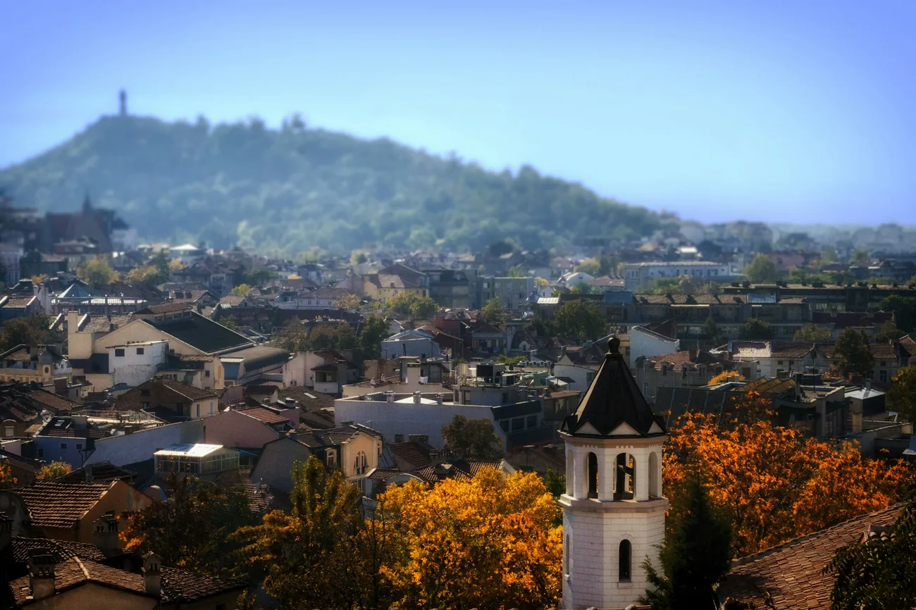Rooftops of Plovdiv with a bell tower, autumn trees and the hill with the monument behind
